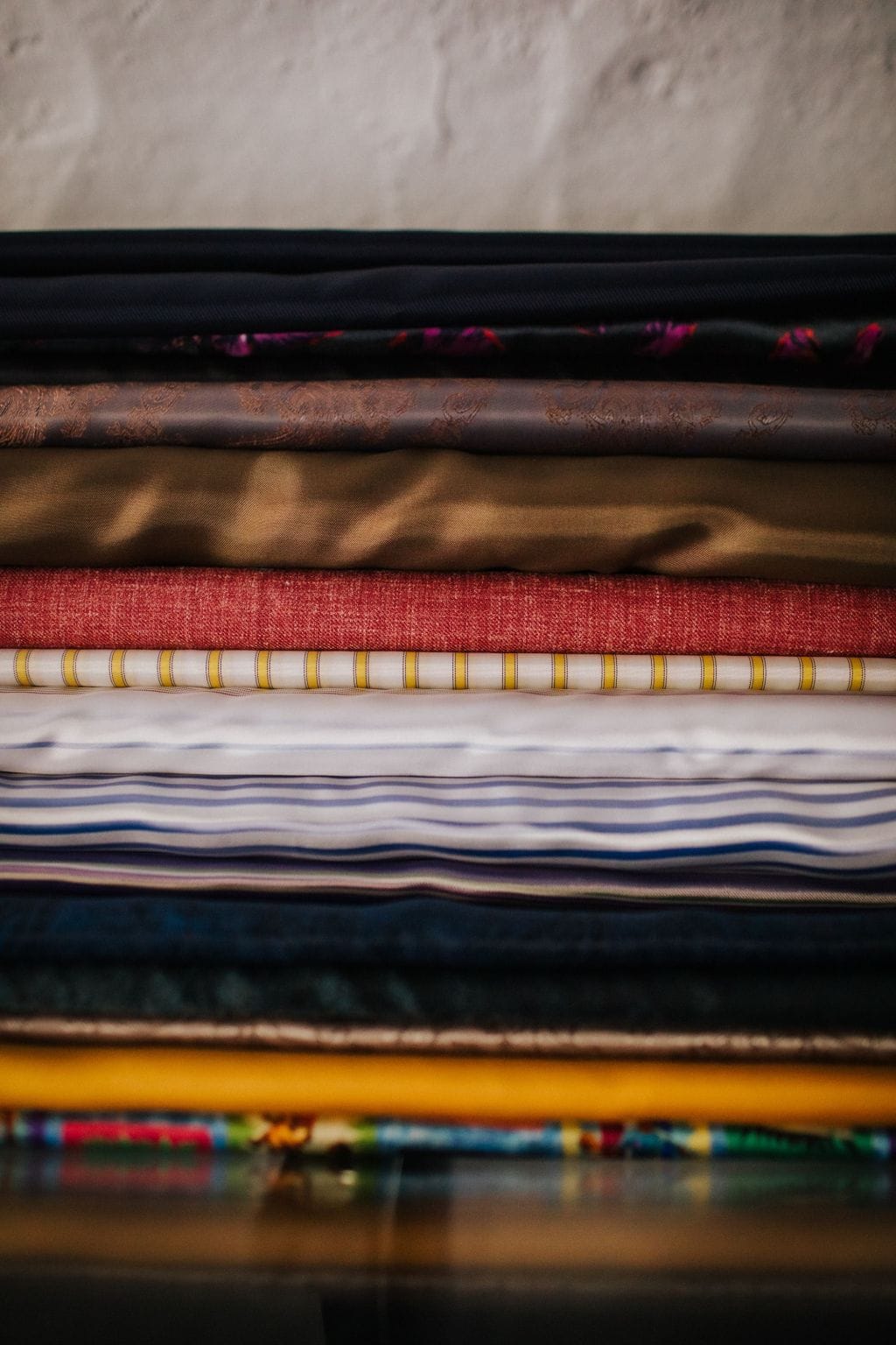 A stack of folded bespoke fabrics — silks, linens, stripes and tweeds — at Souster & Hicks